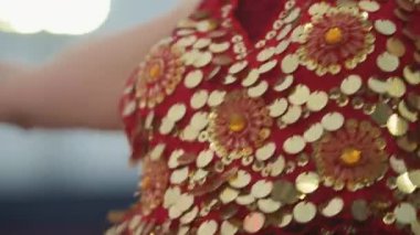 Bir kadın altın boncuklu ve pullu kırmızı bir elbise giyiyor. Kameraya poz veriyor.