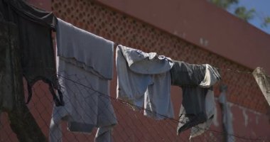 Çitte asılı bir elbise sırası. Giysiler gri ve siyah. Çit metalden yapılmıştır.