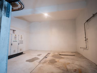 Beyaz duvarı ve gri zemini olan büyük, boş bir oda. Oda boş ve hiç mobilyası yok.