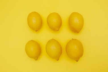 Minimalist düz kompozisyonda altı taze limon, canlı sarı arka planda üç sıra halinde dizilmiş. Parlak ve simetrik yaz konsepti tazeliği, tereddütlü yeme ve doğal turunçgilleri sembolize eder..