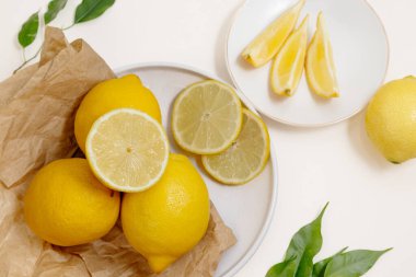 Açık beyaz arka plan üzerine parşömen üzerine yeşil yapraklar yerleştirilmiş taze limonların doğal düz bileşimi. Tazeliği, sağlıklı malzemeleri ve en az tasarımı vurgulayan köylü ve organik gıda kavramı.