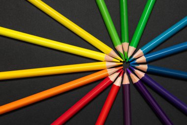 Çok renkli kalemler siyah zemin üzerinde mükemmel bir daire şeklinde dizilmiş, birbirlerine uçlarıyla dokunuyorlar. Birlik, bağlantı, çeşitlilik ve ahengi sembolize eden yaratıcı düz konum.