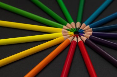 Çok renkli kalemler siyah zemin üzerinde mükemmel bir daire şeklinde dizilmiş, birbirlerine uçlarıyla dokunuyorlar. Birlik, bağlantı, çeşitlilik ve ahengi sembolize eden yaratıcı düz konum.