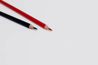 Two pencils, one black graphite and one red colored, positioned in the top left corner of clean white background. Minimal studio composition with strong color contrast and large copy space.