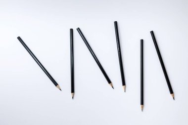 Temiz beyaz zemin üzerine farklı açılara yerleştirilmiş birkaç siyah grafit kalemin yaratıcı düz konumu. Güçlü geometrik çizgileri ve negatif alanı olan minimal tasarım, yaratıcılık, eğitim, basitlik, organiziz kavramları için idealdir