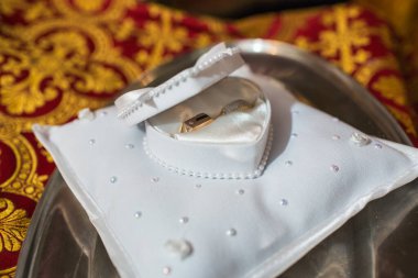 Beyaz Yüzük Yastığında Altın Alyanslar. Altın alyanslar zarif, beyaz bir alyans yastığına yerleştirilmiş boncuklar ve kristaller lüks evlilik geleneğini simgeliyor.