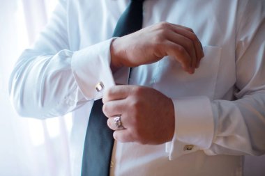 Damat, kelepçeyi evlilik yüzüğüyle ayarlıyor. Damat ellerini kapat kol düğmesini düzelt ve yemin tarzının sembolünü göster ve düğün reklamları için hazırlan erkek giyim ve lüks marka.