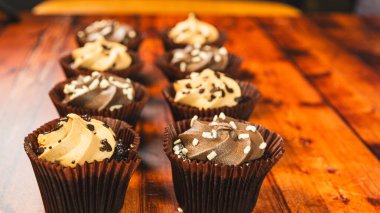 Çikolata ve karamel aromalı çeşitli mini kekler, ahşap bir masada güzelce sergileniyor. Islak, ısırık büyüklüğünde ve partiler, kutlamalar ve tatlı masaları için mükemmel..