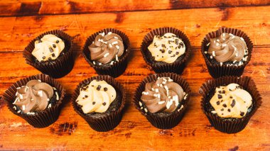 Çikolata ve karamel aromalı çeşitli mini kekler, ahşap bir masada güzelce sergileniyor. Islak, ısırık büyüklüğünde ve partiler, kutlamalar ve tatlı masaları için mükemmel..