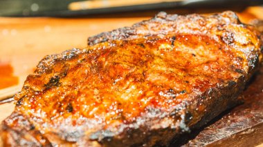 Ender bulunan sulu bir biftek dilimlenmiş ve ahşap bir tahtanın üzerine yerleştirilmiş, içinde pembe bir iç ve karamelize edilmiş kabuk sergileniyor. Yumuşak, lezzetli ve toplantılarda oymak ve hizmet etmek için güzel bir şekilde sunulmuş..