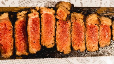 Ender bulunan sulu bir biftek dilimlenmiş ve ahşap bir tahtanın üzerine yerleştirilmiş, içinde pembe bir iç ve karamelize edilmiş kabuk sergileniyor. Yumuşak, lezzetli ve toplantılarda oymak ve hizmet etmek için güzel bir şekilde sunulmuş..