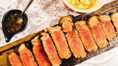 Ender bulunan sulu bir biftek dilimlenmiş ve ahşap bir tahtanın üzerine yerleştirilmiş, içinde pembe bir iç ve karamelize edilmiş kabuk sergileniyor. Yumuşak, lezzetli ve toplantılarda oymak ve hizmet etmek için güzel bir şekilde sunulmuş..