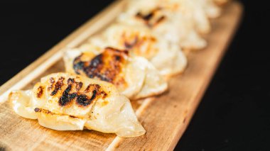 Çok güzel tavada kızartılmış gyoza köftesi, mükemmel altın ve çıtır çıtır, dikdörtgen ahşap bir tahta üzerine dizilmiş. Dalmaya ve eğlenmeye hazır. Paylaşım ve Asya 'dan esinlenilmiş aperatifler için ideal.