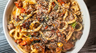 Beautiful beef udon bowl with sesame seeds and fresh vegetables, steaming hot. Rich broth, tender beef, and vibrant colors. Perfect for Japanese comfort food lovers.