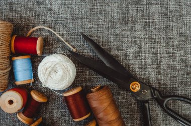 Retro dikiş aletleri: eski makas, gri kumaş üzerindeki iplik bobinleri. Terzinin masası. Tekstil veya ince kumaş üretimi.