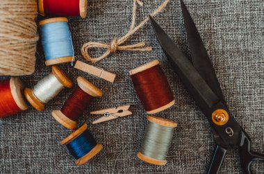 Retro dikiş aletleri: eski makas, gri kumaş üzerindeki iplik bobinleri. Terzinin masası. Tekstil veya ince kumaş üretimi.