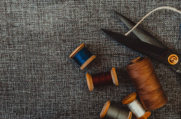 Retro dikiş aletleri: eski makas, gri kumaş üzerindeki iplik bobinleri. Terzinin masası. Tekstil veya ince kumaş üretimi.