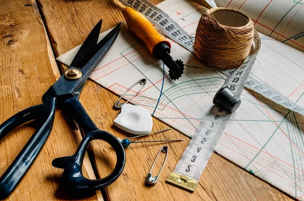 Крупним планом вид ретро швейних інструментів, ножиці, крейда, вимірювальна стрічка лежить на діаграмах хвостовиків і дерев'яному столі Ліцензійні Стокові Зображення