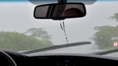 Yağmurlu bir günde yolda araba sürmek, ön camı hızla temizleyen silecek bıçakları. Dikiz aynasından sarkan haçla tespih çekiyorum..