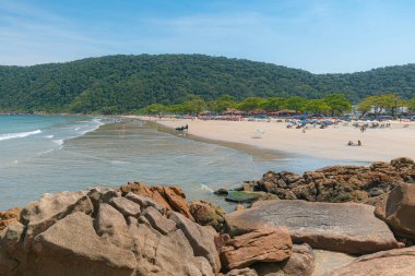 Guaiuba Plajı, Guaruja SP, Brezilya. Sakin denizle küçük körfezin üzerinde güneşli bir gün. Sao Paulo sahilindeki turizm ve boş zamanların görüntüsü. Mata Atlantica bitki örtüsüyle kaplı tepeler manzara.