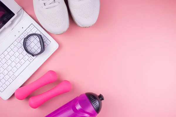 Online fitness. Sneakers, laptop, fitness bracelet, water bottle and dumbbells, on a pink background, workout online.