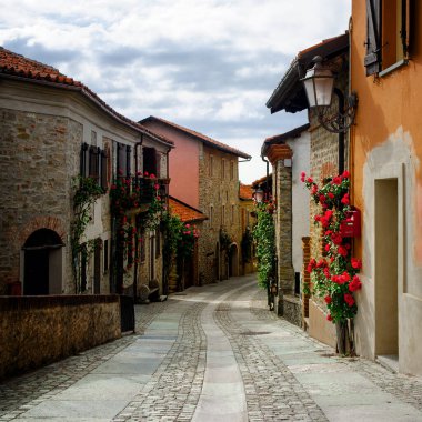 Langhe Hills 'in (Piedmont, İtalya) en çok ziyaret edilen yerlerinden biri olan Bossolasco' nun güzel köyünde dar bir sokak. Kasaba, evler ve balkonların üzerinde büyüyen gülleriyle ünlüdür.