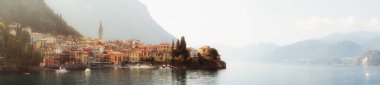 Sabahın erken saatlerinde Varenna, İtalya köyü ile Como Gölü manzarası ve açık gökyüzü, sis, yumuşak güneş ışığı ve uzak dağlar ile