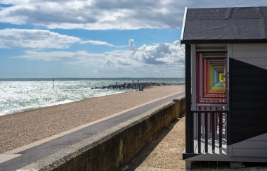 Sol tarafında okyanus ve yukarıda dramatik bulutlu gökyüzü olan deniz kenarındaki gezinti alanı boyunca renkli ahşap kulübeler. Sahil yaz konsepti, seyahat yeri, tatil yaşam tarzı, deniz kenarı mimarisi ve açık hava eğlencesi. İnsan yok, kopyalama alanı.