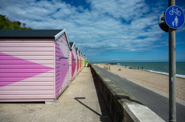 Sol tarafında okyanus ve yukarıda dramatik bulutlu gökyüzü olan deniz kenarındaki gezinti alanı boyunca renkli ahşap kulübeler. Sahil yaz konsepti, seyahat yeri, tatil yaşam tarzı, deniz kenarı mimarisi ve açık hava eğlencesi. İnsan yok, kopyalama alanı.