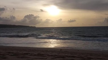 Koyu bulutlar ve altın ışıkla okyanusun üzerinde dramatik bir günbatımı, Endonezya 'nın Bali sahilinde yer alan güçlü bir kıyı manzarası yaratıyor..