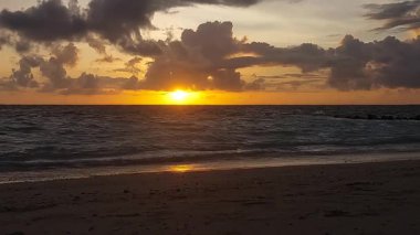 Sakin bir deniz ve kumlu sahil üzerinde alçak güneş, Endonezya, Bali 'deki Kelan plajında sıcak ve rahatlatıcı bir günbatımı sahnesi yaratıyor..