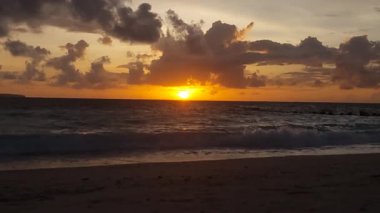 Sakin bir deniz ve kumlu sahil üzerinde alçak güneş, Endonezya, Bali 'deki Kelan plajında sıcak ve rahatlatıcı bir günbatımı sahnesi yaratıyor..