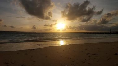 Parlak altın gün batımı okyanus yüzeyine yansıyarak Endonezya, Bali 'deki Kelan plajında sıcak ve huzurlu bir sahil atmosferi yaratıyor..