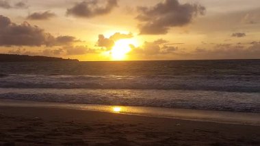 Koyu bulutlar ve altın ışıkla okyanusun üzerinde dramatik bir günbatımı, Endonezya 'nın Bali sahilinde yer alan güçlü bir kıyı manzarası yaratıyor..