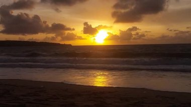 Koyu bulutlar ve altın ışıkla okyanusun üzerinde dramatik bir günbatımı, Endonezya 'nın Bali sahilinde yer alan güçlü bir kıyı manzarası yaratıyor..