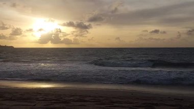 Parlak altın gün batımı okyanus yüzeyine yansıyarak Bali, Kedonganan sahilinde sıcak ve huzurlu bir sahil atmosferi yaratıyor..