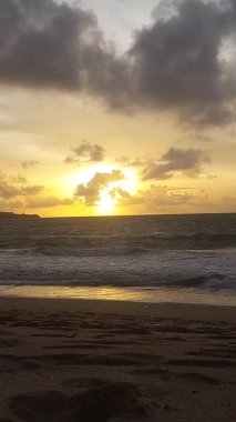 Parlak altın gün batımı okyanus yüzeyine yansıyarak Bali, Kedonganan sahilinde sıcak ve huzurlu bir sahil atmosferi yaratıyor..