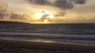 Parlak altın gün batımı okyanus yüzeyine yansıyarak Bali, Kedonganan sahilinde sıcak ve huzurlu bir sahil atmosferi yaratıyor..