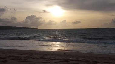 Parlak altın gün batımı okyanus yüzeyine yansıyarak Bali, Kedonganan sahilinde sıcak ve huzurlu bir sahil atmosferi yaratıyor..