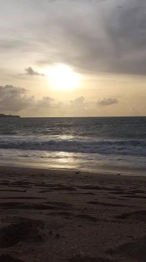 Parlak altın gün batımı okyanus yüzeyine yansıyarak Bali, Kedonganan sahilinde sıcak ve huzurlu bir sahil atmosferi yaratıyor..