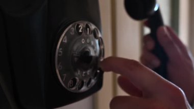 Klasik bir siyah çevirmeli telefon kullanarak, arama yapmak için nabzı atan bir telefon numarası çevirerek. Dönen kadranın mekanik hareketi ve dokunsal etkileşim nostalji, retro teknoloji ve analog iletişimi çağrıştırıyor..