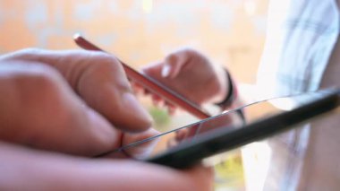 Yakın plan video, akıllı telefonlar kullanırken iki kişinin yüzünü gösteriyor. Sahne modern sosyal etkileşim, dijital iletişim ve günlük mobil teknoloji kullanımını yakalar.