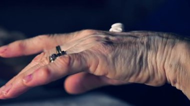 Nemlendirici krem sürerken parmaklarında yüzük ve vitiligo olan yaşlı kadın elleri. Cilt bakımı, cilt bakımı, cilt bakımı, cilt hastalıkları farkındalığı, yaşlanma ve kişisel bakım kavramı. Gerçekçi yaşam tarzı görüntüleri doku ve jestlere odaklı.