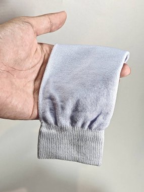 İnsan elinin beyaz örülmüş kumaş kolunun veya çorabın kumaş ve esnekliğini gösteren profesyonel bir stüdyo resmi. Tarafsız bir arkaplanda, tıbbi, tekstil veya giyim pazarlama için ideal..