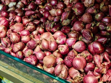 Bir marketteki soyulmamış kırmızı soğan yığınının yakından, yüksek açılı görüntüsü. Görüntü, soğanların kağıt dokusunu ve canlı mor derilerini gösteriyor. Yemek pişirmek ya da sağlıklı bir yaşam tarzı için mükemmel.