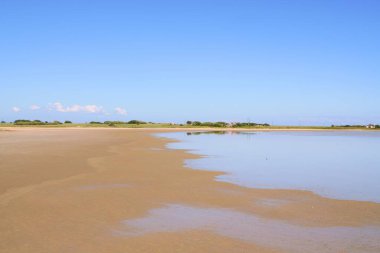 Alyki tuzlu gölü kumlu sahil ve durgun su mavi gökyüzünü yansıtıyor.