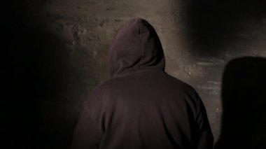 Karanlık bir istasyon odasında polis sorgusu sırasında kameraya geri dönen isimsiz bir kapüşonlu hacker. Siber suçlar soruşturması, kanun uygulama sorgulaması, gizlilik.