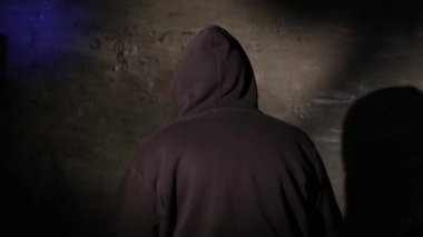 Karanlık bir istasyon odasında polis sorgusu sırasında kameraya geri dönen isimsiz bir kapüşonlu hacker. Siber suçlar soruşturması, kanun uygulama sorgulaması, gizlilik.