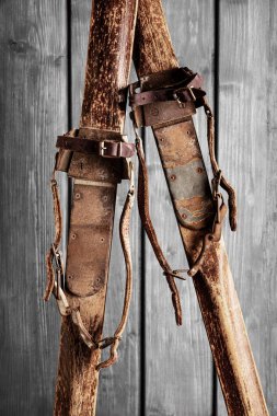 Gri ahşap arka planda deri kayaklarla bağlanmış antik ahşap kayaklar.
