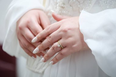 Gelinin manikürlü elleri beyaz elbisesinin önünde alyanslarını gösteriyor.